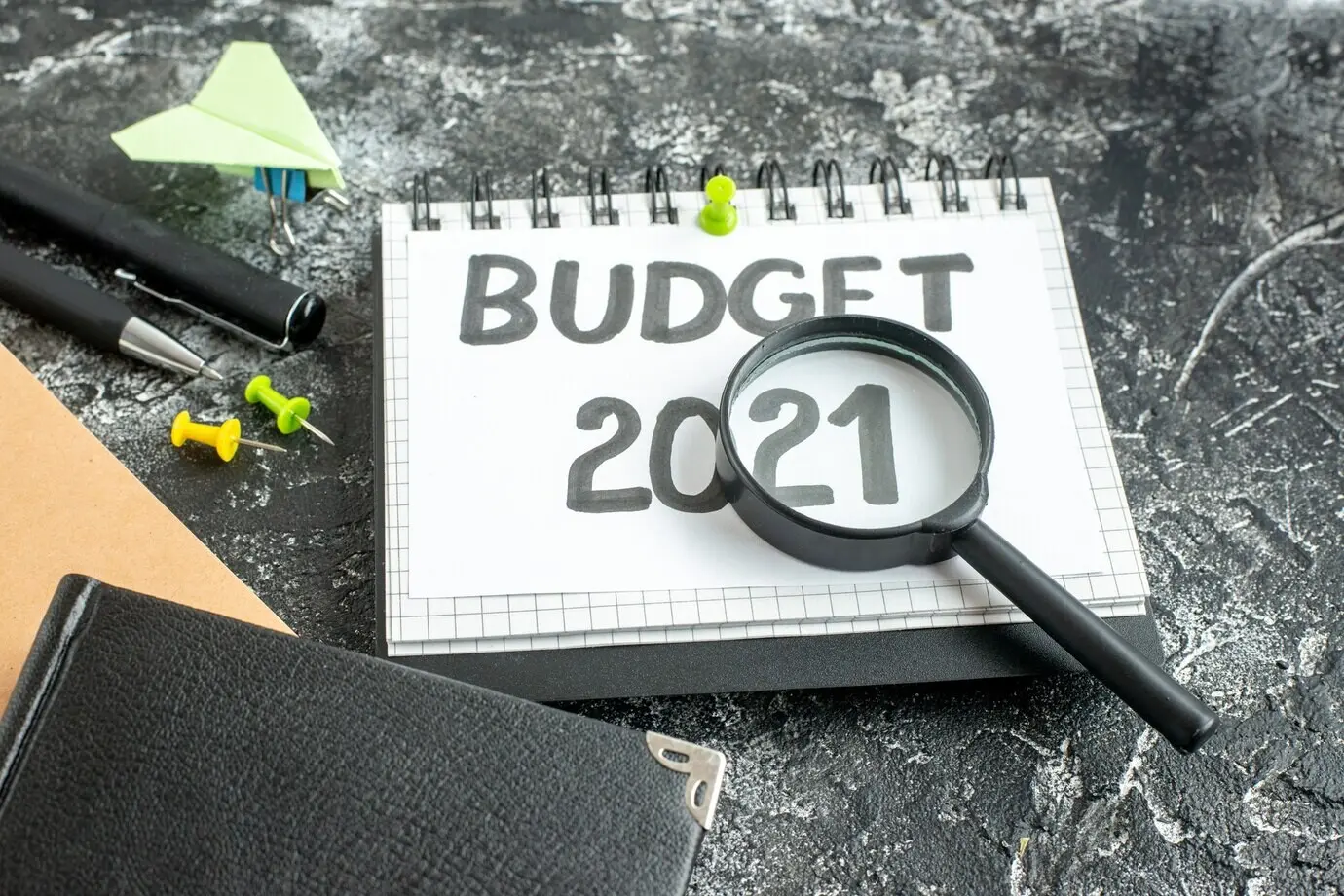 Vorderansicht einer Budgetnotiz mit Stiften und Lupe vor dunklem Hintergrund.